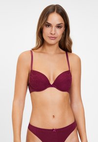 Bordeaux kant beha met gewatteerde cups, verstelbare bandjes en een klein satijnen strikje in het midden. Soepele textuur, onderbreuningssteun.