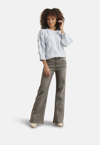 Light blue cable-knit sweater with a round neck, paired with high-waisted gray flared jeans. The sweater features textured diamond patterns.