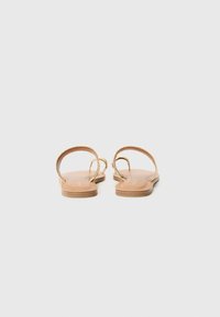 Flache Sandalen verfügen über zwei schlanke Riemen, eine abgerundete Zehenpartie und eine glatte Lederoberfläche mit einer leichten Sohle. Sichtbare goldene Akzentbeschläge.