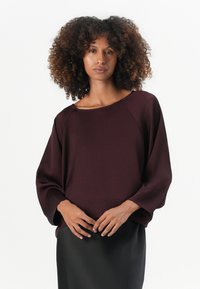 Pull bordeaux en maille douce, avec un large col, des manches chauve-souris et une coupe décontractée, associé à une jupe noire.
