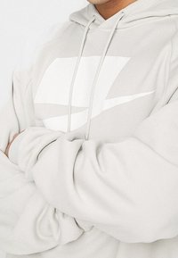 Ljusgrå hoodie med en vit geometrisk design framtill, med snoddar och ribbade ärmslut. Mjukt, texturerat tyg.