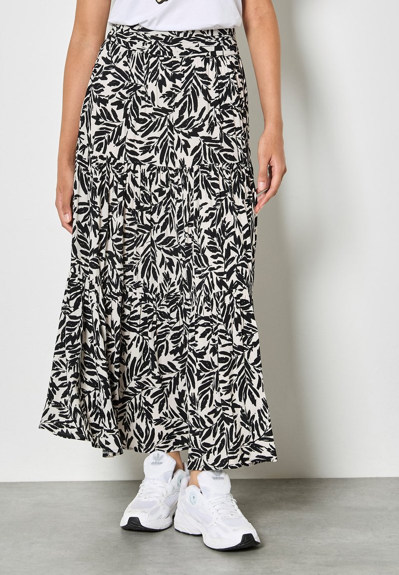 Jupe midi à motif de feuilles noir et blanc avec un design à volants et une taille élastique, portée avec des baskets blanches de sport.