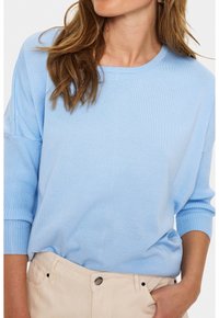 Maglione azzurro chiaro a maglia con polsini a coste e scollatura rotonda, abbinato a pantaloni beige. Il tessuto sembra morbido e leggermente strutturato.