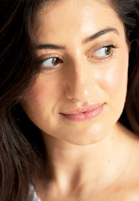 Close-up van een gezicht met een medium huidskleur, warme ondertonen, donker golvend haar en natuurlijke make-up gericht op de ogen en lippen.