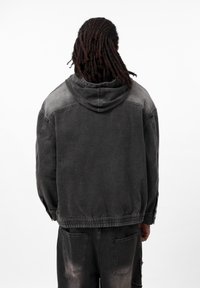Zwarte denimjas met een capuchon, voorzien van een gradient vervaging, elastische manchetten en een ontspannen pasvorm. Minimalistisch ontwerp zonder zichtbare hardware.