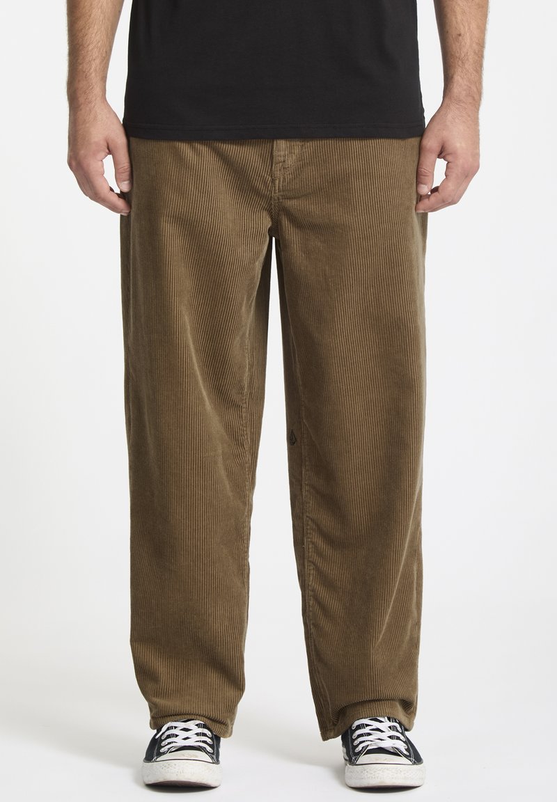 Brune fløjlsbukser med en bred, afslappet pasform. Lodret ribbet tekstur og sidelommer, kombineret med sorte sneakers.