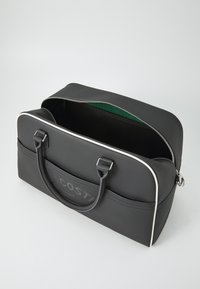 Borsa duffel nera realizzata in materiale testurizzato, con un logo prominente, rifiniture bianche e doppi manici. L'apertura con zip rivela un interno verde.