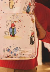 Ružový batoh so illustrations Paddingtona Medveďa, zlatými kovovými doplnkami a štítkom Cath Kidston. Ozdobený farebnými vzormi a konfietami.