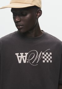 Dark gray cotton t-shirt featuring a large white graphic design with stylized letters and a checkered pattern on the left side.