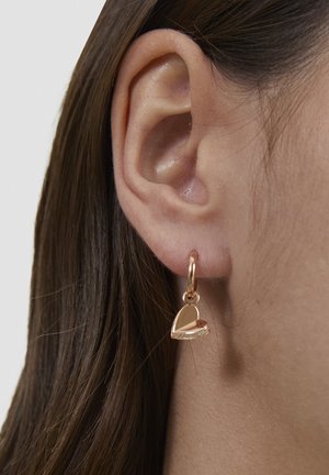 Ørering i rosaguldfarvet hjerteformet bøjle med en glat finish, hængende fra en lille cirkulær lås, placeret nær øret.