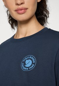 Navyblauwe katoenen t-shirt met een ronde, lichtblauwe Fjällräven-logo inclusief tekst. Zachte textuur, klassieke ronde halslijn, geen zichtbare patronen.