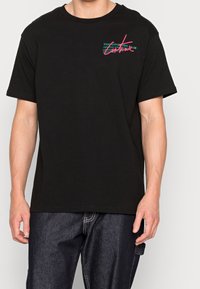 Camiseta de algodón negra con mangas cortas, que presenta un texto gráfico de colores en el pecho. Corte regular, diseño de cuello redondo.
