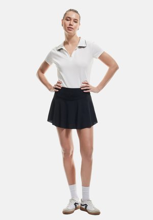Polo shirt bianco a maniche corte con colletto nero, abbinato a una gonna svasata nera e calze bianche. Modello che indossa sneakers in stile retro.