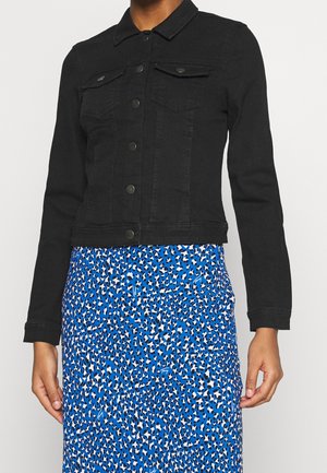 Black buttoned denim jacket with two chest pockets worn over a blue and black spotted patterned skirt.