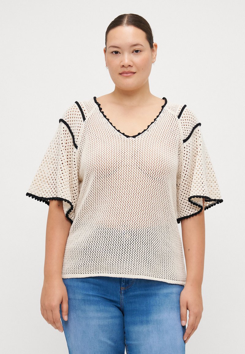 White mesh top with black scalloped edges, wide bell sleeves, and a V-neckline, featuring intricate open-knit detailing throughout.
