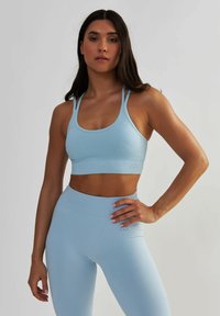 Jasnoniebieski stanik sportowy z wysokim dekoltem i cienkimi ramiączkami; zestawiony z dopasowanymi legginsami o wysokim stanie, posiadającymi prążkowaną strukturę.