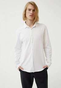 Wit overhemd met lange mouwen van lichtgewicht stof, met een kraag en knopen aan de voorkant, gedragen met een donkere broek.