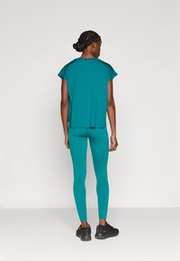 Σετ αθλητικής ένδυσης σε τυρκουάζ χρώμα που περιλαμβάνει μια φαρδιά μπλούζα με κοντά μανίκια και στενά κολάν, κατασκευασμένα από ένα απαλό, ελαστικό ύφασμα.