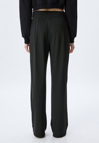 Zwarte, wijde broek met een gladde textuur, elastische tailleband en een minimalistisch ontwerp. Geen zichtbare patronen of extra hardwaredetails.