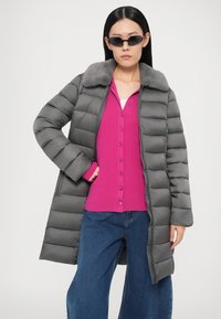 Halli paksud talvejope kunstkarvaga kraega, sobitatud erkroosa nööbitava särgiga. Märgatavad laiad teksapüksid ja stiilsed mustad päikeseprillid.