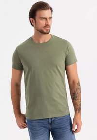 T-shirt verde oliva a maniche corte in un tessuto morbido, con scollatura a girocollo e vestibilità regolare. Il modello indossa jeans in denim.