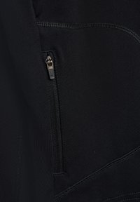 Close-up van zwarte stof met zichtbare ritszak en gedetailleerde stiksels op kledingmateriaal.