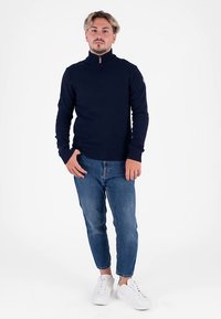 Maglione lavorato a maglia blu navy con collo alto, abbinato a jeans azzurri e sneakers bianche. Il maglione presenta un orlo e polsini a costine.
