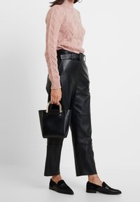 Maglione lavorato a maglia rosa chiaro con collo alto e motivo in pizzo, abbinato a pantaloni in pelle nera, mocassini neri e una piccola borsa nera.
