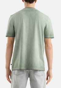 T-shirt à rayures vertes à manches courtes avec un col rond, tissu texturé et ourlet droit, porté avec un jean gris clair.