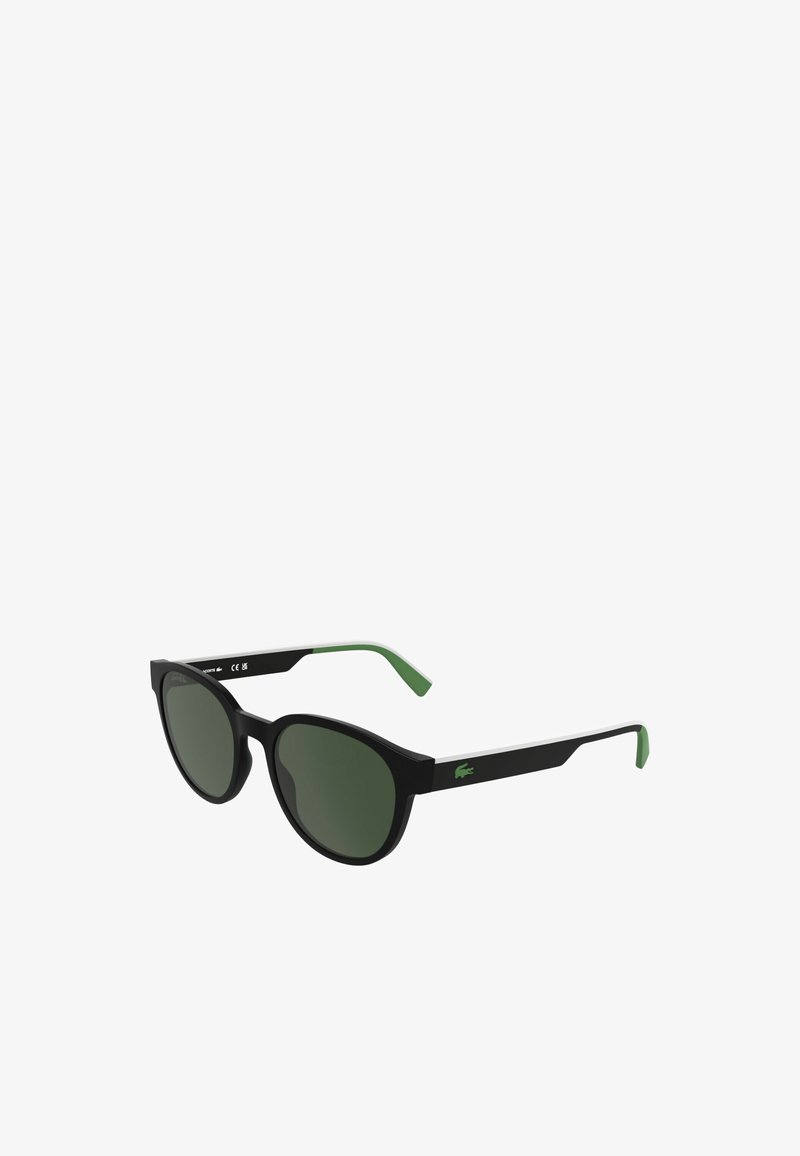 Lunettes de soleil noires avec accents verts, verres ovales et logo distinct sur la branche. Matériau léger, design bicolore avec des détails blancs.