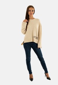 Maglione beige in maglia con maniche larghe e la scritta "AMORE" stampata sull'orlo, abbinato a jeans skinny blu scuro e scarpe con tacco nere.