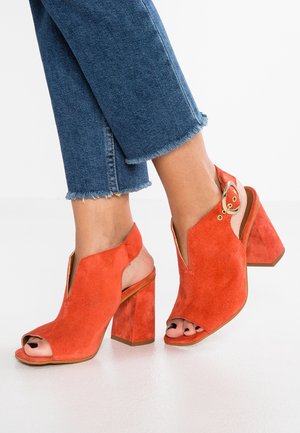 Sandały na obcasie, otwarte z przodu, sięgające do kostki, wykonane z pomarańczowego zamszu z masywnym obcasem. Bocznie wycięcia i złote akcenty podkreślają design.