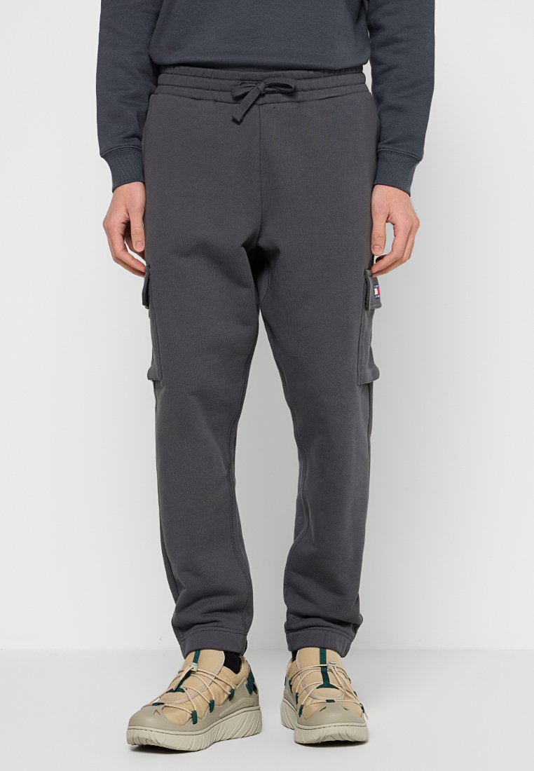 Grå fleece-joggare med dragsko i midjan, sidofickor och ribbade muddar, tillsammans med beige skor med gröna detaljer.
