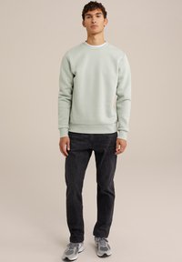 Light green crew-neck sweatshirt in a soft material, paired with dark jeans and grey sneakers; features ribbed cuffs and hem.
