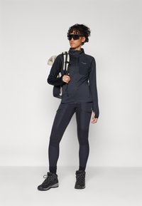 Black athletic jacket with a zippered front and a chest pocket, paired with black patterned leggings and sturdy black hiking boots.