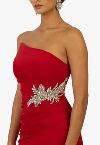 Abito rosso senza spalline con dettagli arricciati e un'applicazione floreale in argento in vita. Realizzato in un tessuto liscio e elasticizzato.