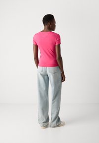 Klevende roze T-shirt met korte mouwen en een ronde hals, gecombineerd met een lichte blauwe straight-leg jeans en witte sneakers. Eenvoudig ontwerp zonder patronen.