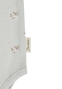 Hellgrauer Body mit kleinen Blumenmustern in Weiß und Beige, der eine weiche, glatte Textur aufweist und ein Seitenlabel mit dem "Stemtaler"-Logo hat.