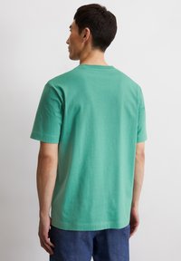 T-shirt in cotone verde con maniche corte e design a girocollo, texture liscia e vestibilità rilassata, vista da dietro.