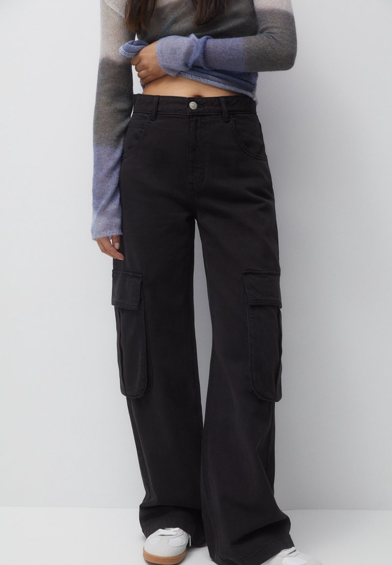 Zwarte cargo broek met wijde pijpen, voorzien van zijzakken en een knoopsluiting. De stof heeft een soepele, duurzame textuur.
