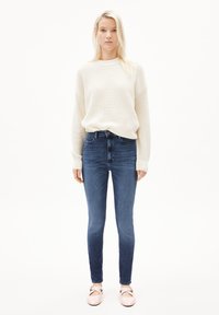 Suéter de canalé marfil de corte holgado, combinado con jeans ajustados de color azul oscuro. Bailarinas rosas claras con tiras entrecruzadas completan el look.