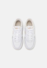 Białe skórzane sneakersy z perforowanym noskiem, płaskimi sznurowadłami i kremowym akcentem po boku. Posiadają teksturowane wnętrze i gumową podeszwę.