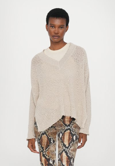 Beige knitted sweater with a V-neck, long sleeves, and a loose fit; paired with patterned leggings in shades of brown and black.
