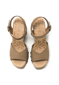 Sandalias de cuero marrón con una correa ancha en el dedo del pie, correa en el tobillo y un patrón decorativo de hojas en la plantilla; suela plana con pequeños remaches negros.