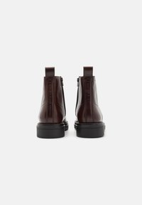 Bottes Cheville en cuir marron avec une finition lisse, des zips sur les côtés et des semelles en caoutchouc noir robustes. Équipées de languettes au niveau des talons.