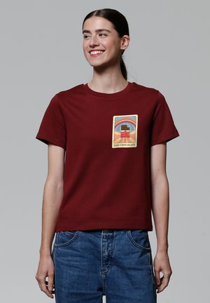 T-shirt en coton bordeaux avec un col ras-du-cou et des manches courtes. Présente un design graphique sur le devant, mettant en avant un thème chocolat.