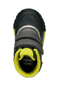Zapato negro y gris con correas de Velcro, acentos verdes y un interior texturizado amarillo. Presenta un talón reforzado y una suela de goma.
