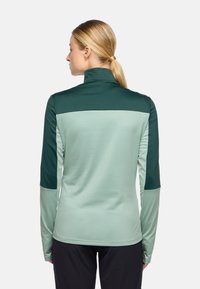 Langärmliges Sportshirt in einem hellgrünen und dunkelgrünen Farbblockdesign, aus glattem, flexiblem Stoff mit hohem Kragen.