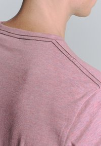 Roze t-shirt met korte mouwen van een zachte stof, met een ronde halslijn en contrasterende stiksels langs de schoudernaad.