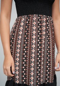 Robe noire et multicolore présentant un corsage froncé, une jupe à volants à motifs floraux et circulaires, et un tissu léger.